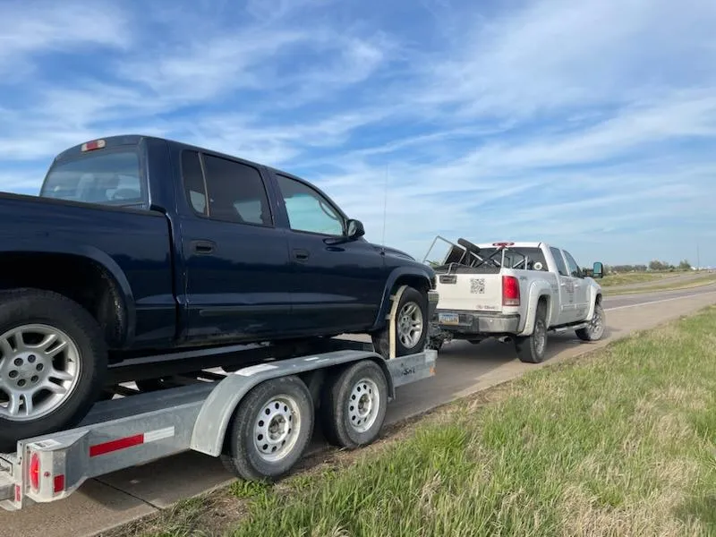 Pickup pulling a car on a flatbed trailer down a country road